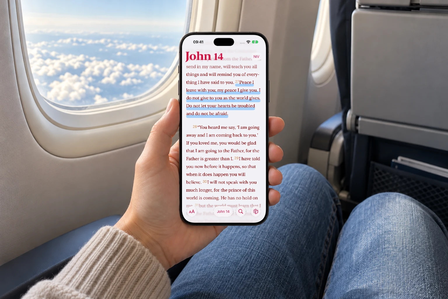 An iPhone displaying John 14 beside an airplane window